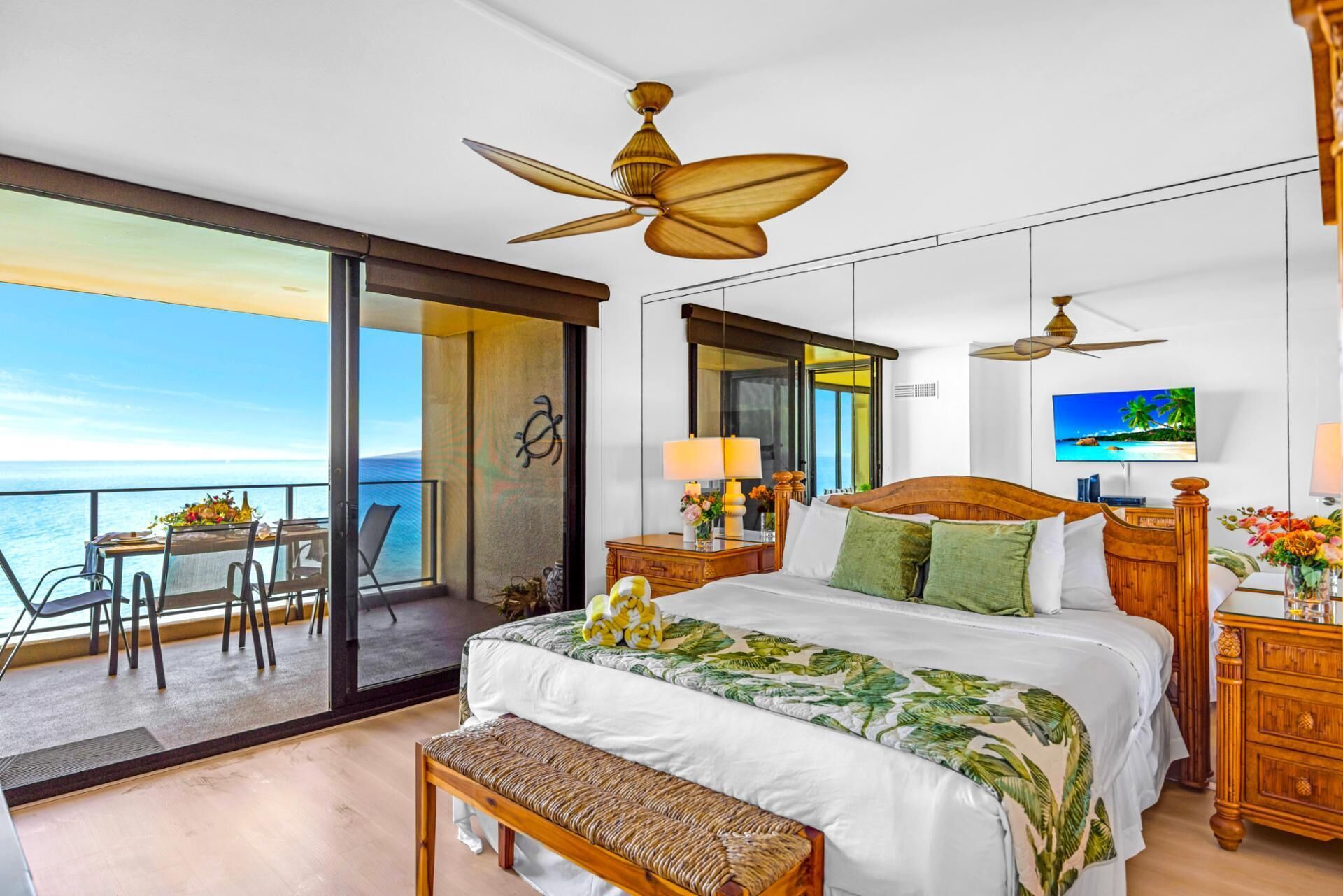 A spacious bedroom with a large bed, a balcony with a view of the sea, and a television on the wall.