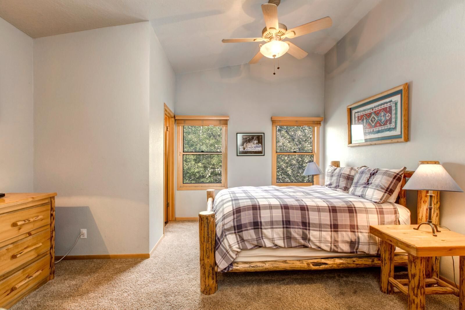 A bedroom with a bed, a nightstand, a dresser, and two windows.