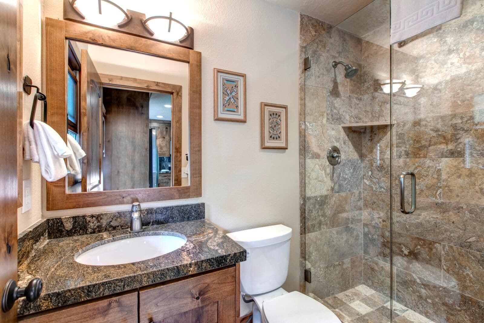 Une salle de bain avec un lavabo sur un plan de travail en granit, des toilettes blanches, une douche en verre et un meuble-lavabo en bois.