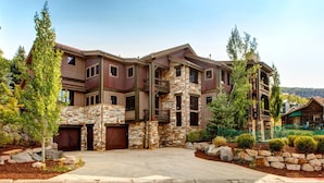 A multi-story house with a stone facade, multiple garage doors, and a landscaped driveway. - Rossi Hill 4 Bedrooms PRH-685 by KBM (Park City)