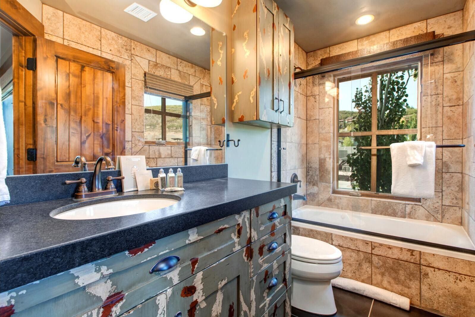 Un bagno con parete in pietra, porta in legno, lavandino con rubinetto e water.
