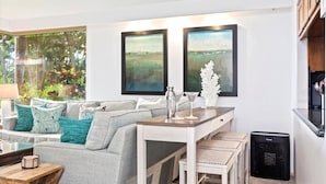 Una sala de estar con un sofá, una mesa de centro y una mesa de comedor con sillas. Hay dos cuadros en la pared, un pequeño adorno blanco y un calefactor negro en el suelo.