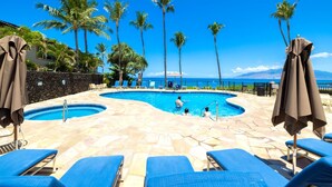 Zona de piscina con sillas de descanso, palmeras y vista al océano.
