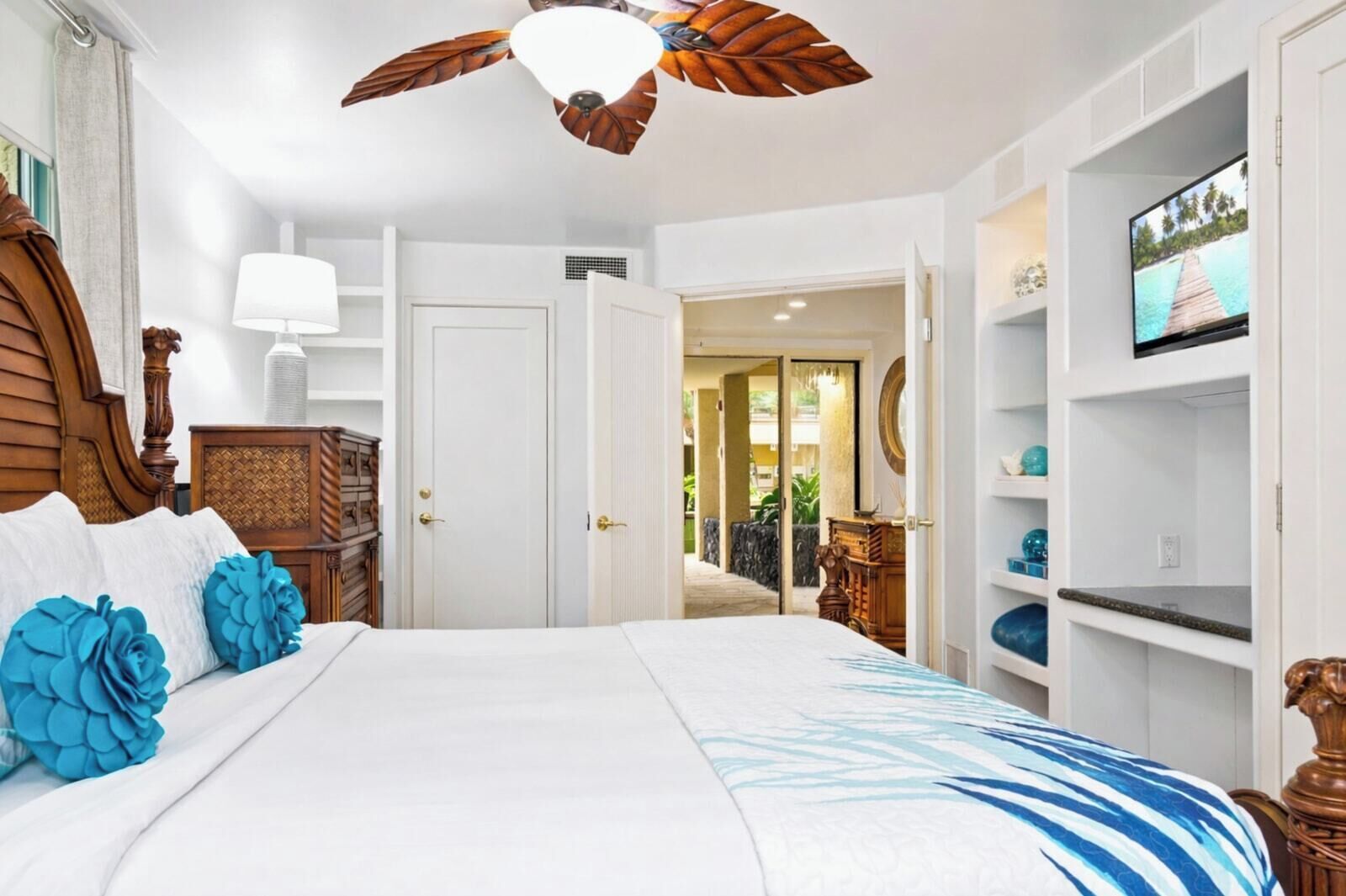A bedroom with a large bed, a ceiling fan, a TV, and a view of the outdoors.