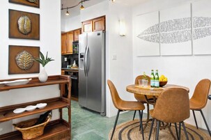 Une cuisine moderne dotée d’un réfrigérateur en acier inoxydable, de meubles en bois et d’un coin repas avec une table ronde et des chaises marron.