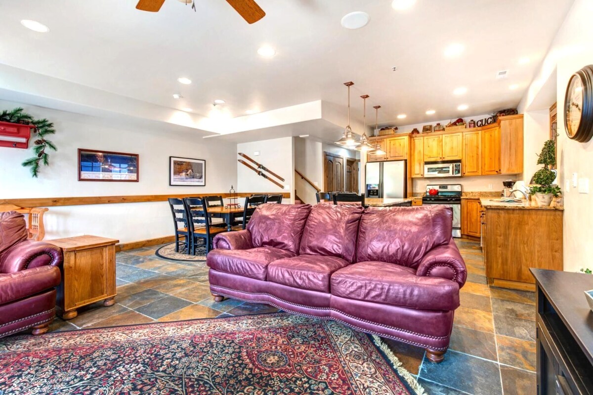 A spacious living room with a purple leather sofa, a patterned rug, and a dining area with wooden chairs.