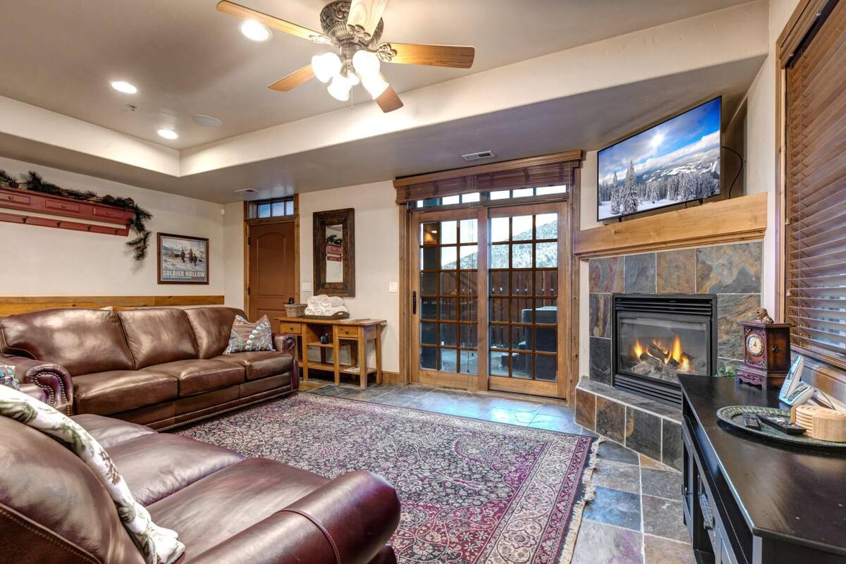 Ein gemütlicher Wohnraum mit Ledersofa, Kamin und großem Fenster mit Blick auf schneebedeckte Bäume.