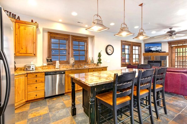A kitchen with wooden cabinets, a stainless steel dishwasher, a granite countertop, and a dining area with a table and chairs.