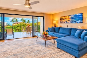 Un salón con un sofá azul, una mesa de centro de vidrio y vistas a un jardín tropical a través de amplios ventanales correderas.