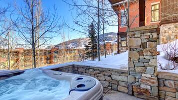 A hot tub in a stone-walled outdoor area with a view of a building and trees.