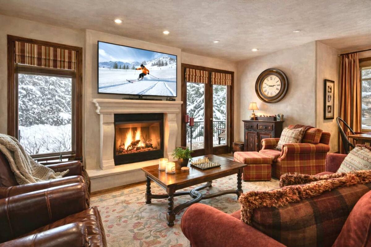 Ein gemütliches Wohnzimmer mit Kamin, Fernseher und Blick auf eine verschneite Landschaft.