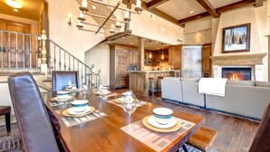 A dining area with a wooden table set for four, a fireplace, and a staircase leading to another level. - Vintage on the Strand by KBM (Park City)