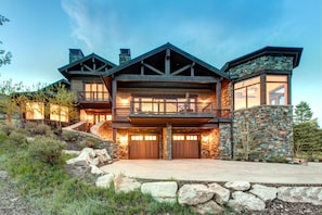 A large, multi-story house with a stone exterior, multiple balconies, and a driveway.