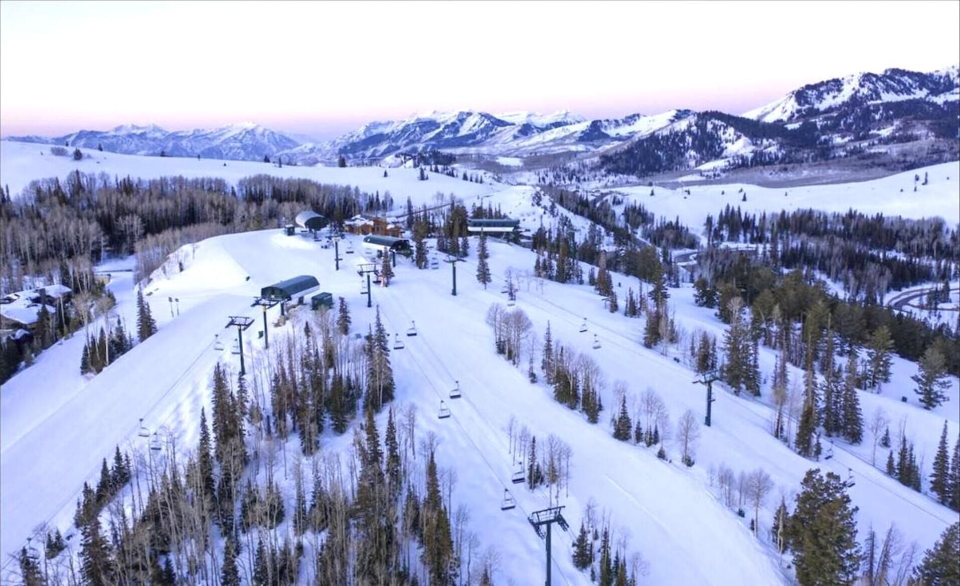 Ein schneebedecktes Skigebiet mit Seilbahnen, Gebäuden und Bergen im Hintergrund.