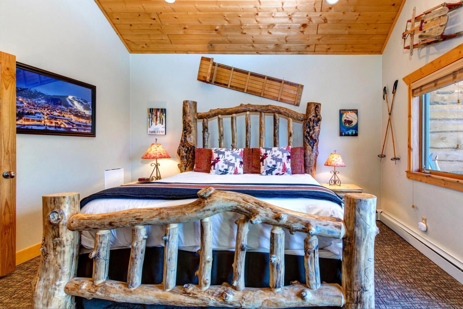 A bedroom with a rustic wooden headboard, a cityscape painting, and a window with a view.