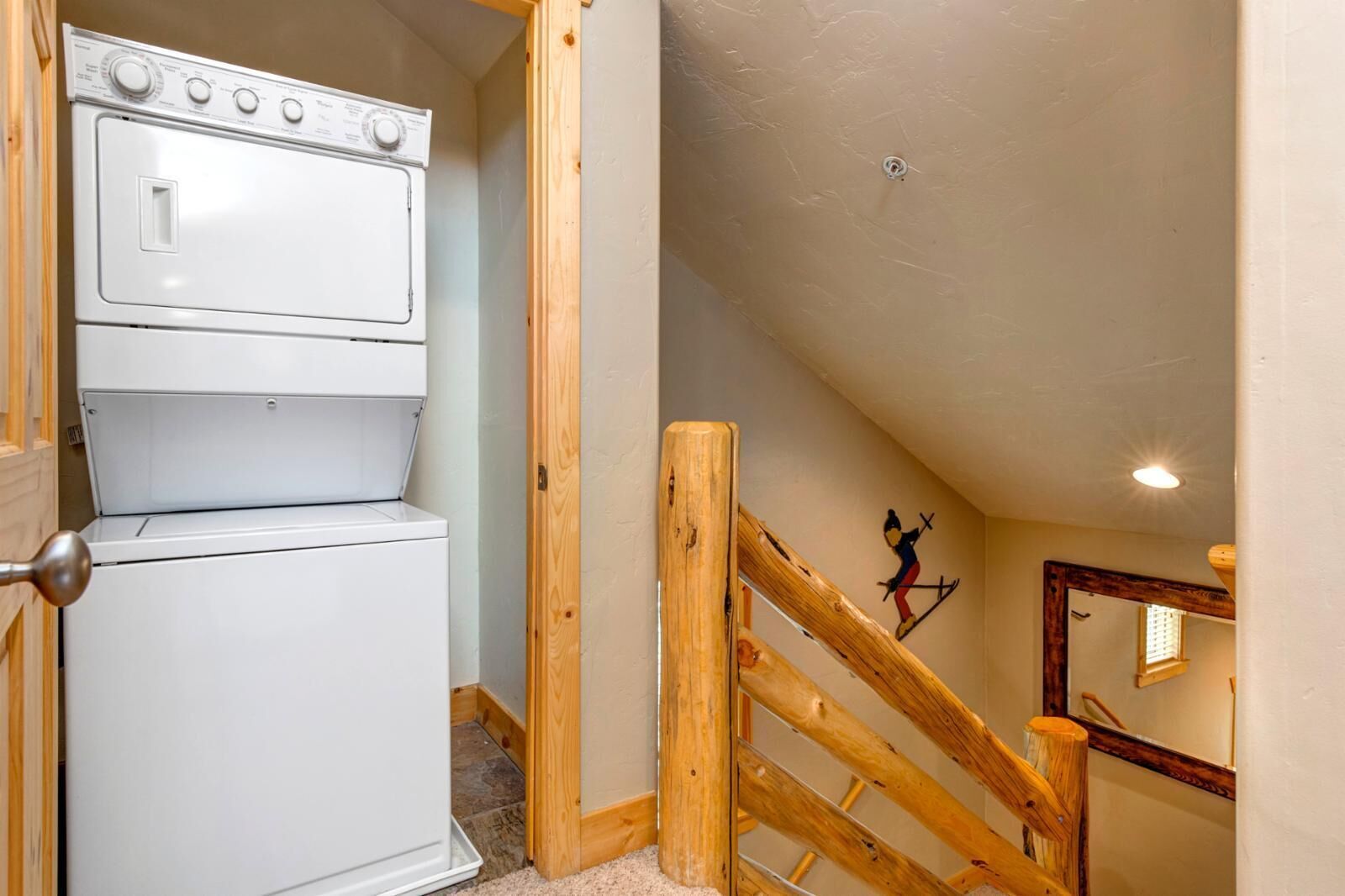 A laundry room with stacked dryers and a wooden staircase leading to an upper level.