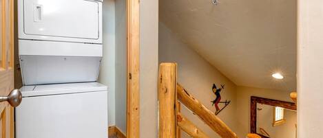 A laundry room with stacked dryers and a wooden staircase leading to an upper level.