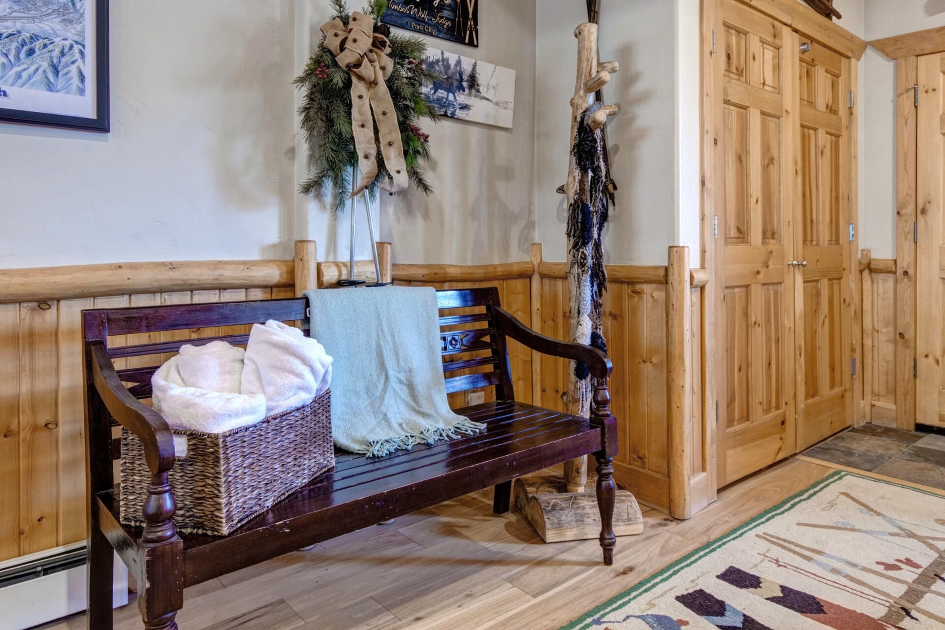 A wooden bench with a woven basket and towels, a wooden door, and a patterned rug.