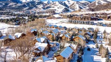 A snow-covered village with wooden houses and a ski resort in the background.
