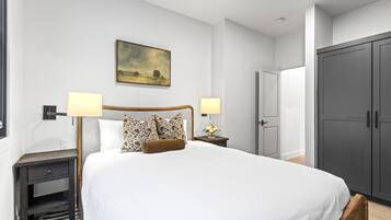 A bedroom with a large bed, two bedside lamps, a nightstand, a painting on the wall, and a wardrobe.
