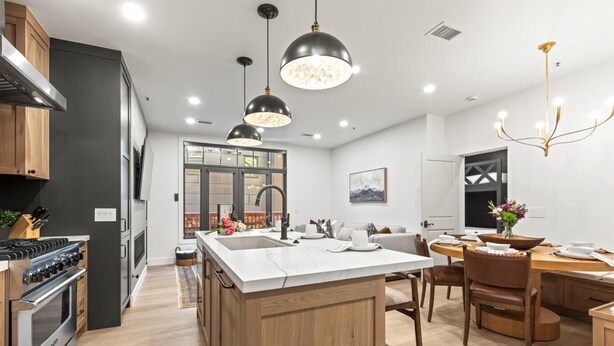 Una cocina moderna con una isla central, armarios de madera y un comedor con candelabro.