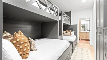 A modern bedroom with bunk beds, a wooden headboard, and a kitchen area visible through an open door.