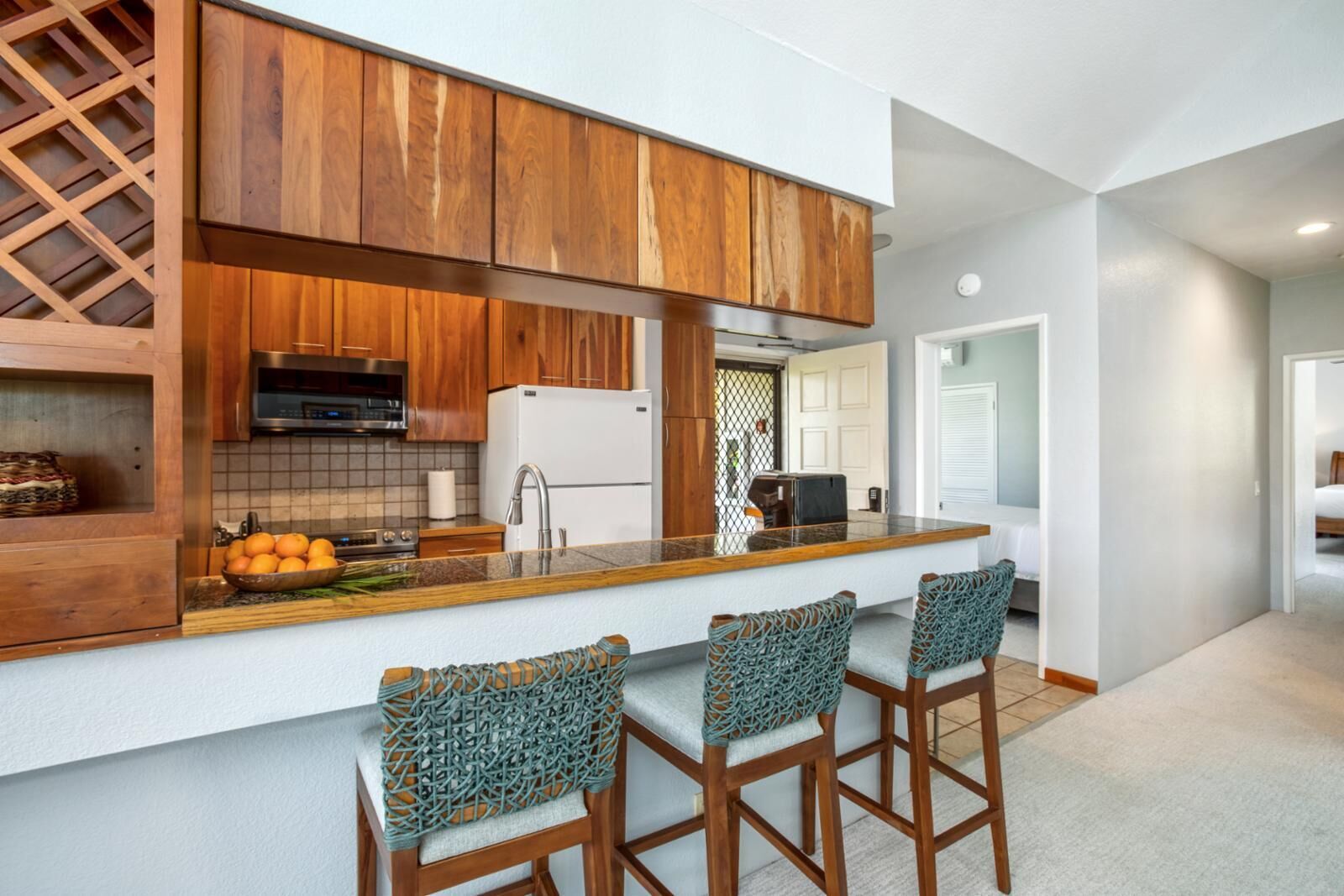 A modern kitchen with wooden cabinets, a built-in oven, a refrigerator, and a bar area with stools.