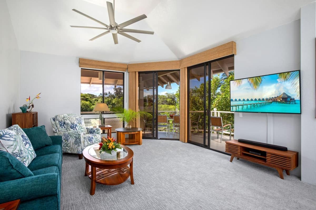 A spacious living room with a teal sofa, a coffee table, and a TV mounted on the wall.