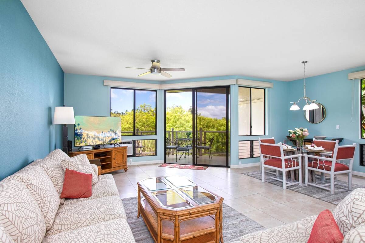 A living room with a sofa, coffee table, and dining area with chairs. There is a ceiling fan and a painting on the wall.