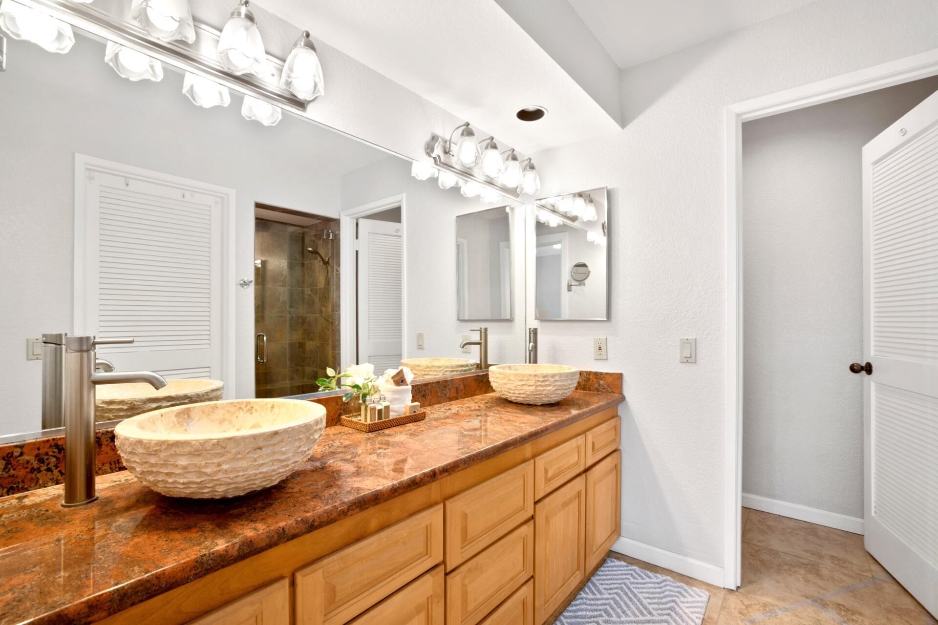 Une salle de bain avec deux grands lavabos ronds de couleur beige, un meuble-lavabo en bois et un grand miroir avec des lumières au-dessus.