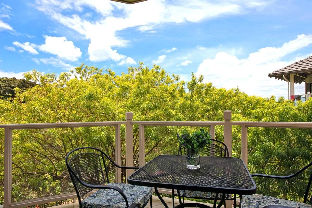 An outdoor patio with a table and chairs, surrounded by a wooden railing, overlooking a lush green landscape.