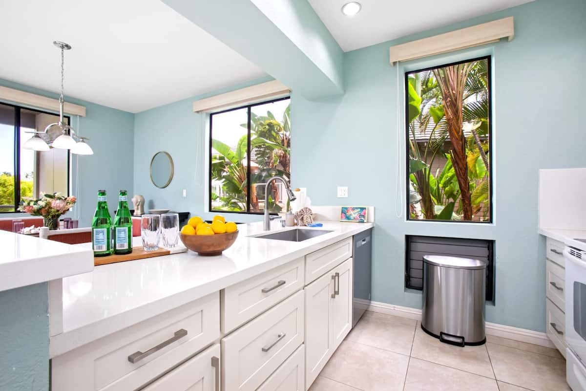 A modern kitchen with a large window, a sink, and a trash can.