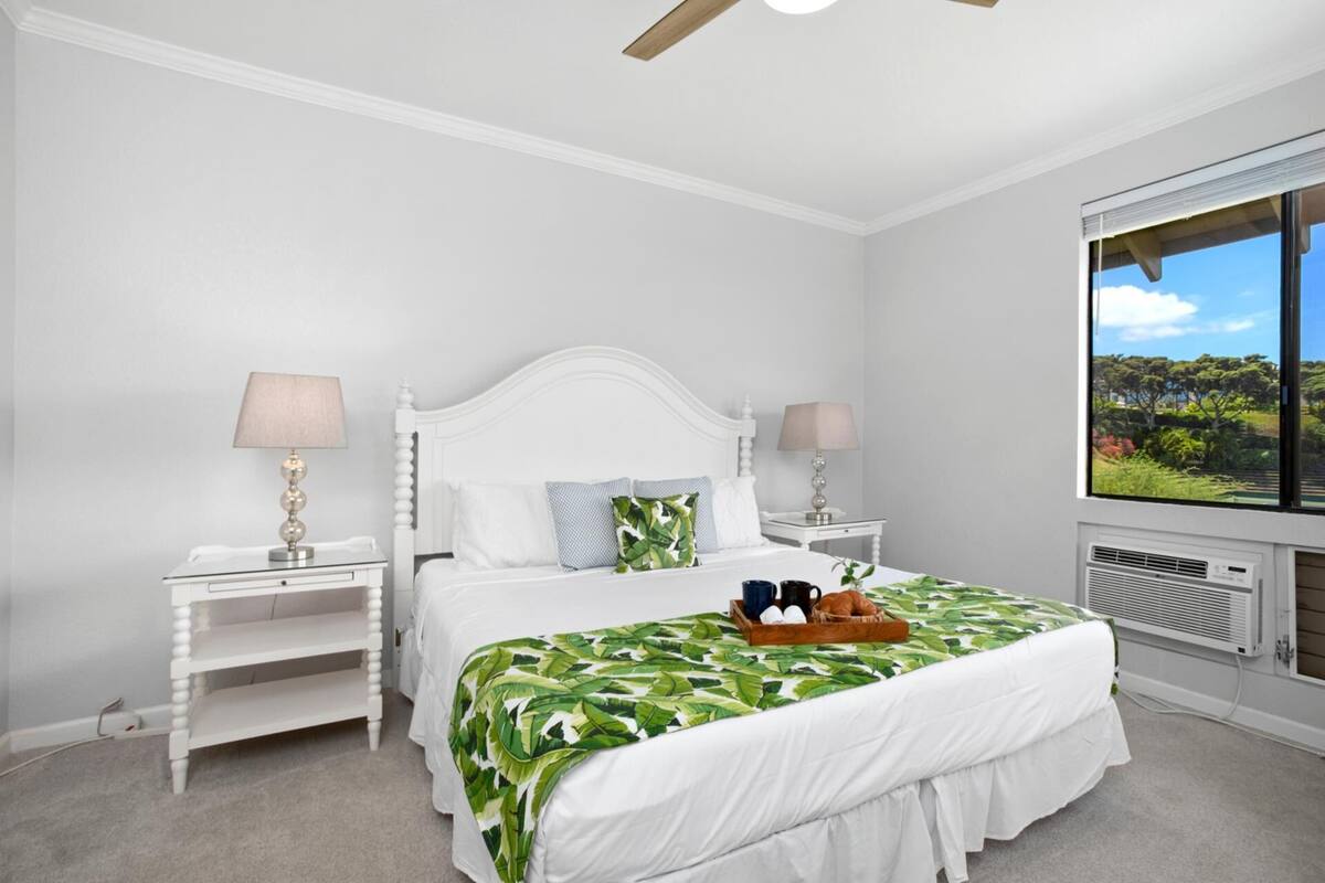 A bedroom with a bed, two bedside tables, a window with a view, and a ceiling fan.