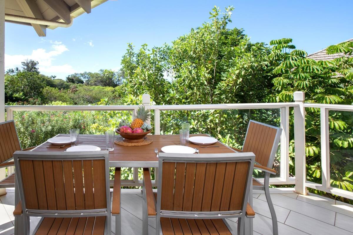 A wooden deck with a table set for four, surrounded by chairs, and a bowl of fruit on the table.