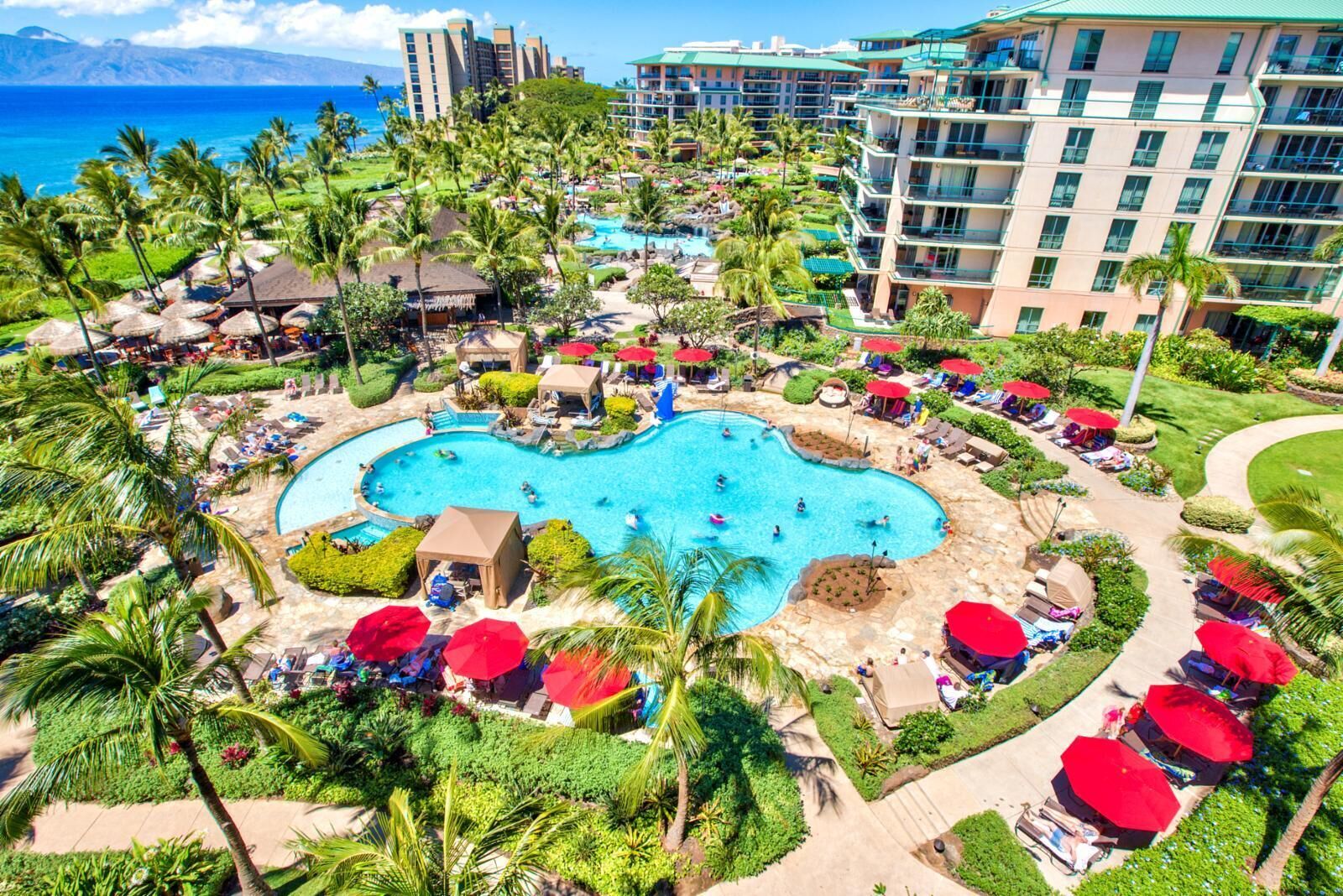 A resort with a large central pool surrounded by palm trees and lounge areas.