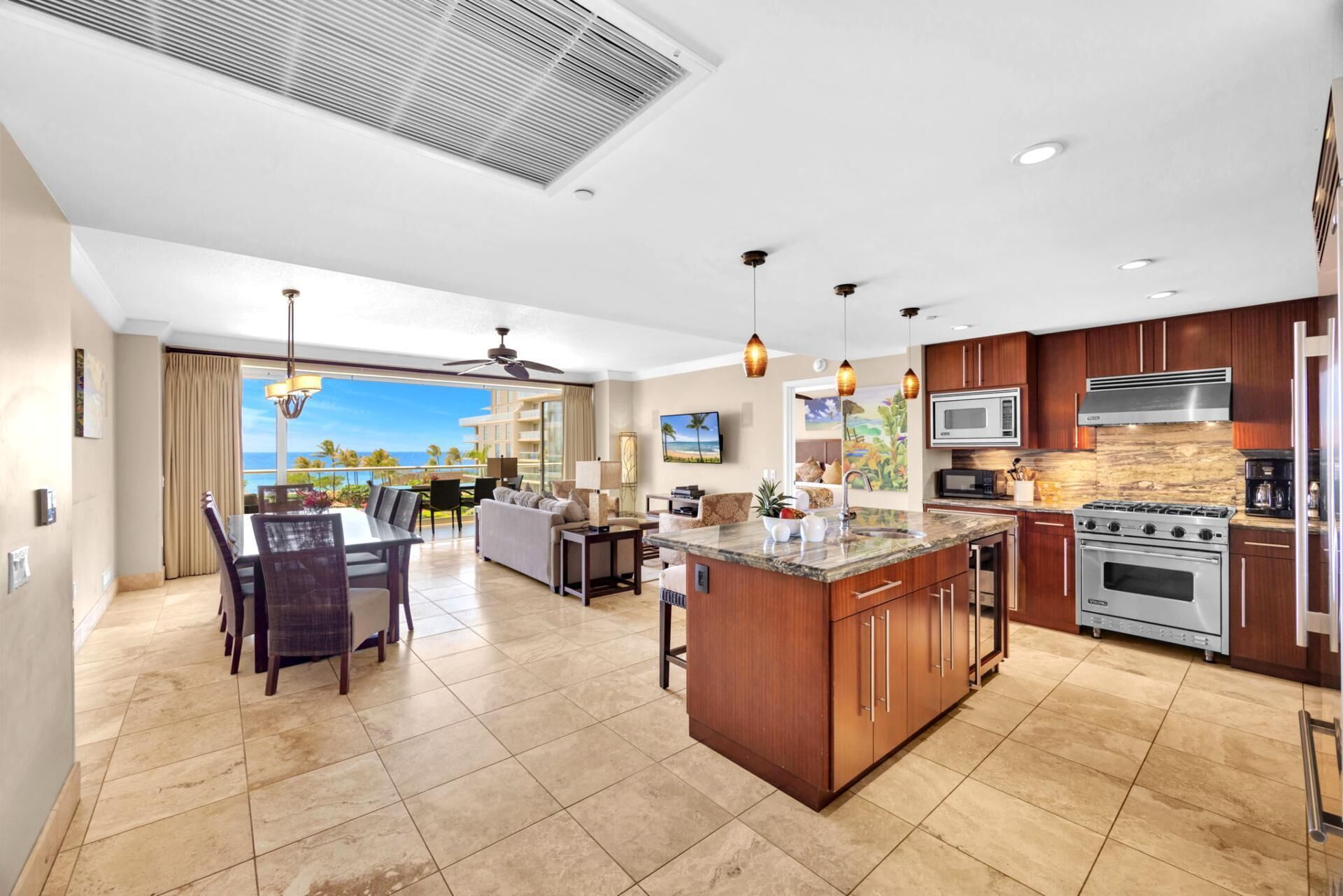 A spacious kitchen with a central island, a dining area with a view, and a living room with a large window overlooking the ocean.