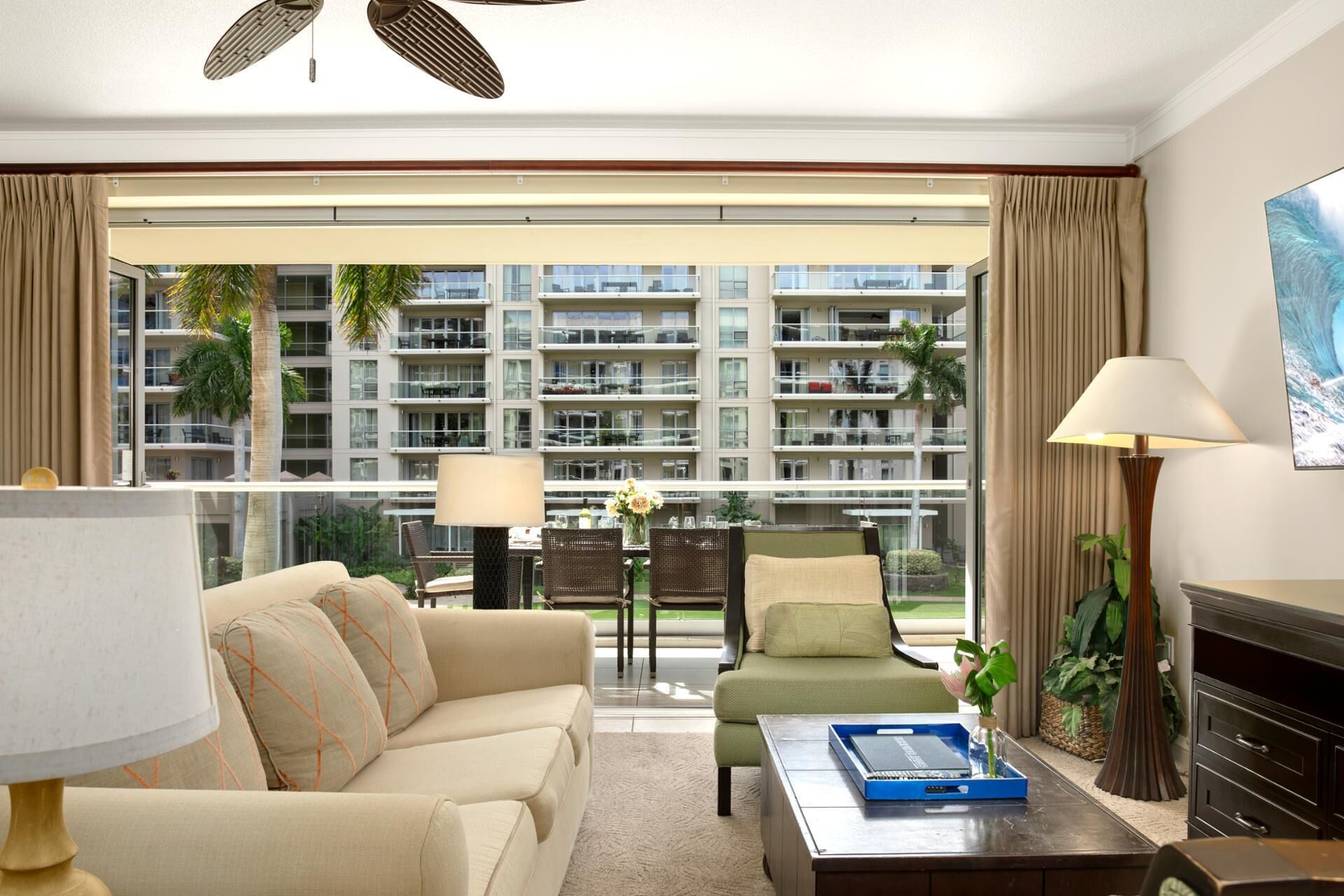 Habitación de hotel con sofá, sillón, mesa de centro y vista a un edificio con balcones.