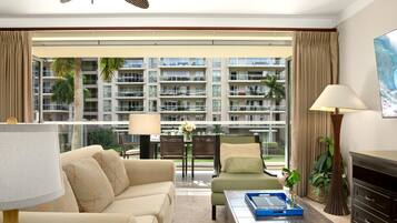 Habitación de hotel con sofá, sillón, mesa de centro y vista a un edificio con balcones.