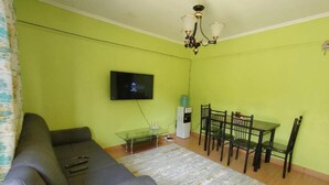 A living room with a sofa, a TV mounted on the wall, a small table with chairs, and a water dispenser. - Stay.Plus Lake View House Naivasha (Naivasha)