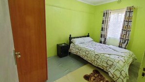 A bedroom with a bed, a nightstand, a window with curtains, and a door. - Stay.Plus Lake View House Naivasha (Naivasha)