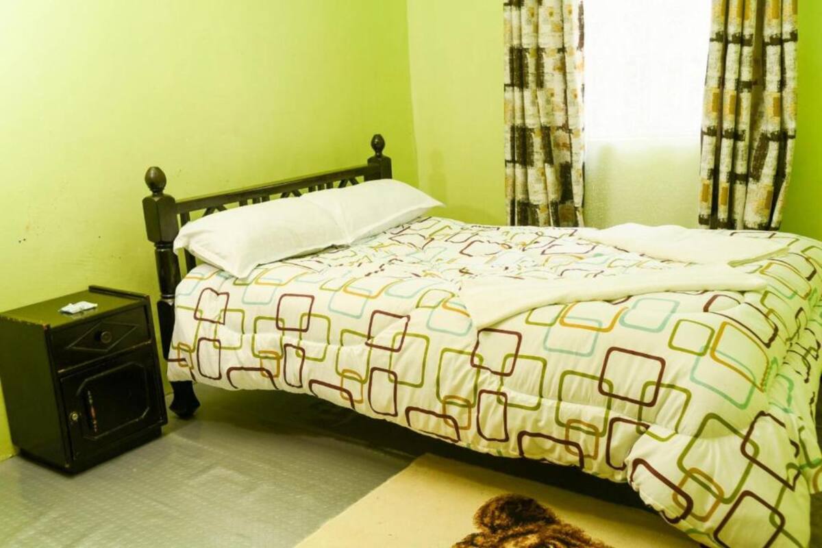 Un lit avec une couvre-lit à motifs, une table de chevet avec une lampe et des rideaux à une fenêtre.