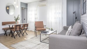 A modern living room with a sofa, a dining table with chairs, a coffee table, and a large mirror. - Incredible 2 Bedroom Apartment at El Rastro (Madrid)