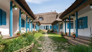 Un patio con un sendero adoquinado, rodeado de edificios con contraventanas azules y techos de paja.