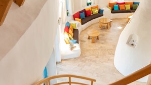 Una escalera de caracol con escalones de madera y barandilla, que conduce a una sala de estar con un conjunto de sofás y una mesa redonda.