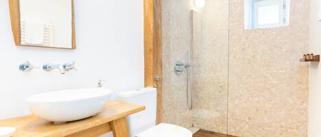 A modern bathroom with a wooden vanity, a large mirror, a white sink, a toilet, and a glass-enclosed shower.