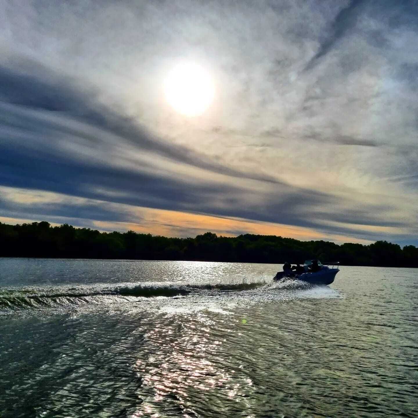 A boat on a calm body of water with a clear sky and sunlight reflecting on the water's surface.