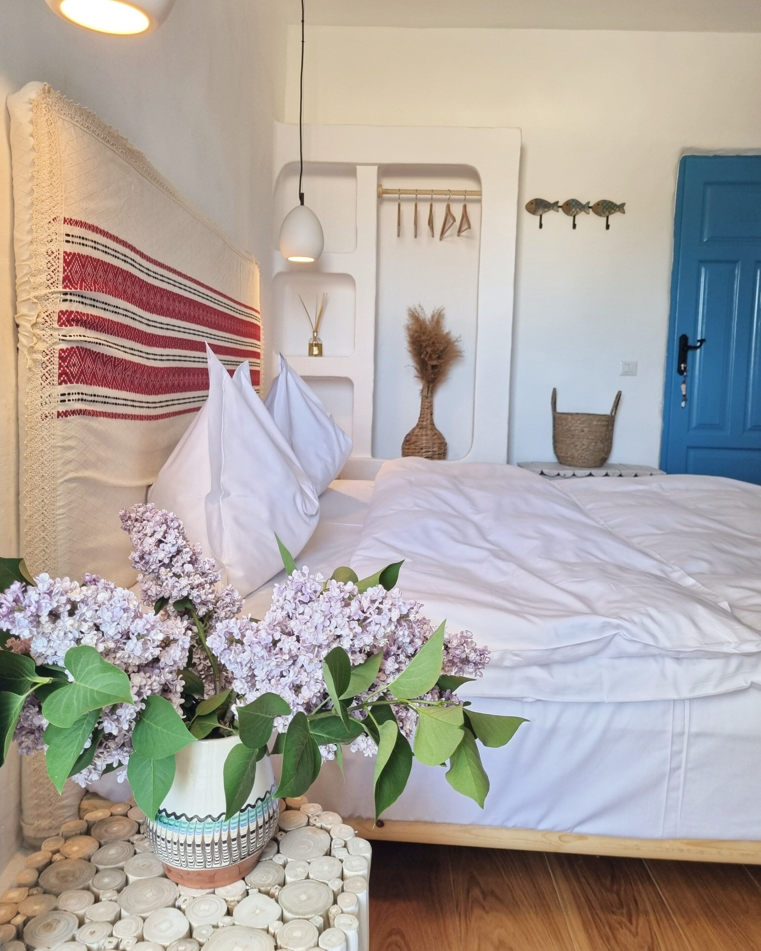 Une chambre à coucher avec un lit, des oreillers, un vase de fleurs, une lampe suspendue, une porte bleue et des décorations murales.
