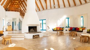 Amplia sala de estar con chimenea central, muebles de madera y una escalera que lleva a un nivel superior.