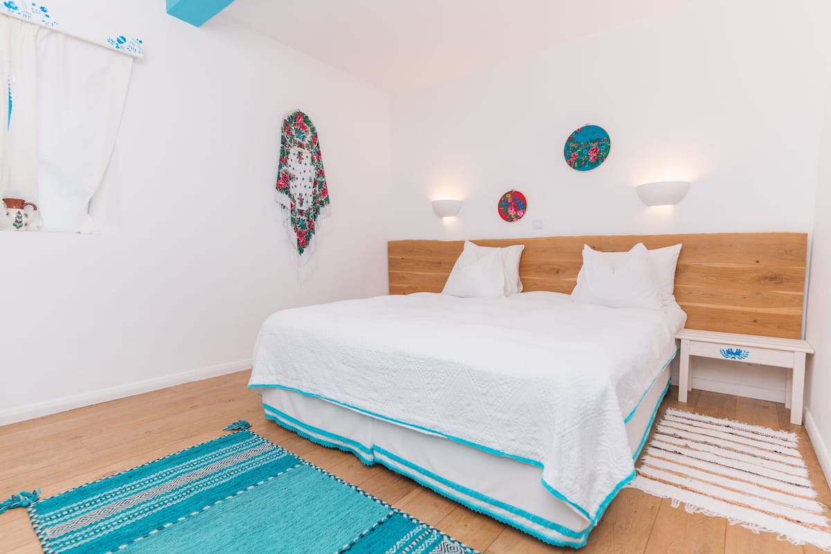 A bedroom with a wooden headboard, white bedding, and a teal and white striped rug.