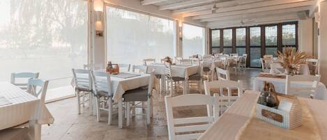 A spacious restaurant with white tables and chairs, large windows, and a view of the outdoors.